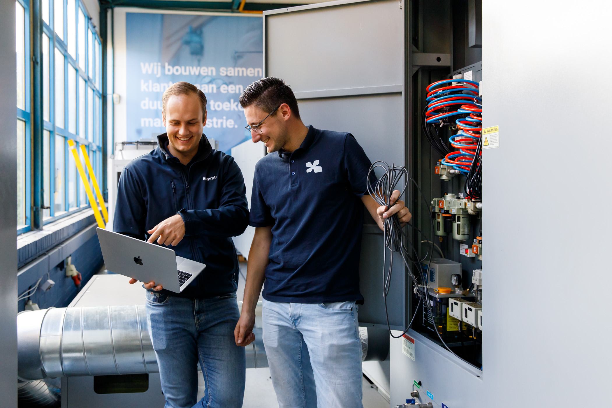 Two Summix colleagues looking at machine data together on a laptop by a control cabinet